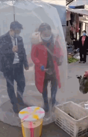 중국에서 한 커플이 몸 전체를 가리는 대형 비닐 우산을 쓴 채 장을 보고 있다./사진=트위터