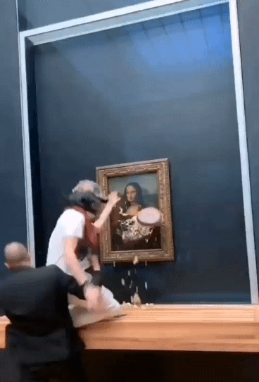 29일(현지시간) 한 남성이 할머니 분장을 하고 프랑스 루브르박물관에 전시된 세계적인 명작 '모나리자'에 케이크를 던져 쫓겨나고 있다./사진=트위터 갈무리