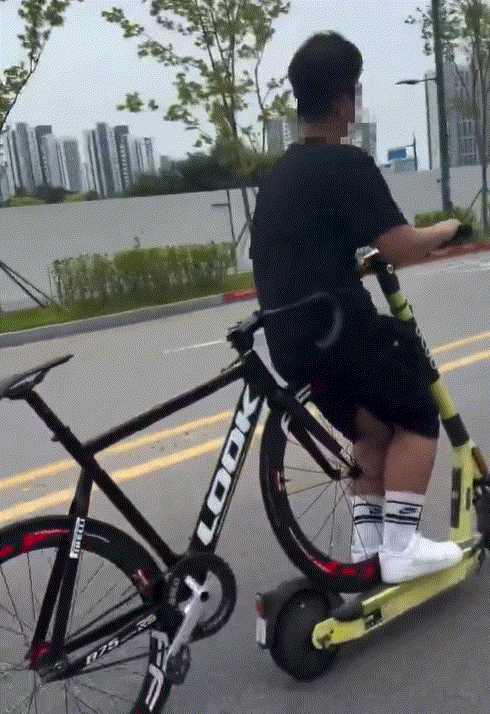전동킥보드 위에 자전거를 걸친 채 도로를 주행하는 남성의 모습이 포착돼 안전 불감증 논란이 일고 있다./사진=SNS 갈무리