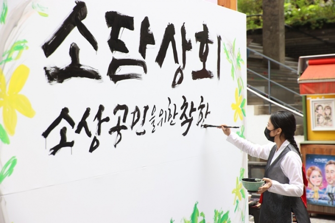 방역당국이 단계적 일상 회복을 앞두고 사회적 거리 두기를 2주 더 연장하자 자영업자 단체들은 마지막 거리 두기 조치가 돼야 한다고 강조했다. 사진은 '소상공인 플래그십 스토어' 개장행사에서 명인의 대형 붓글씨 연출로 코로나19로 지친 소상공인을 위로하는 광고물 모습. /사진=뉴스1(중소벤처기업부 제공)