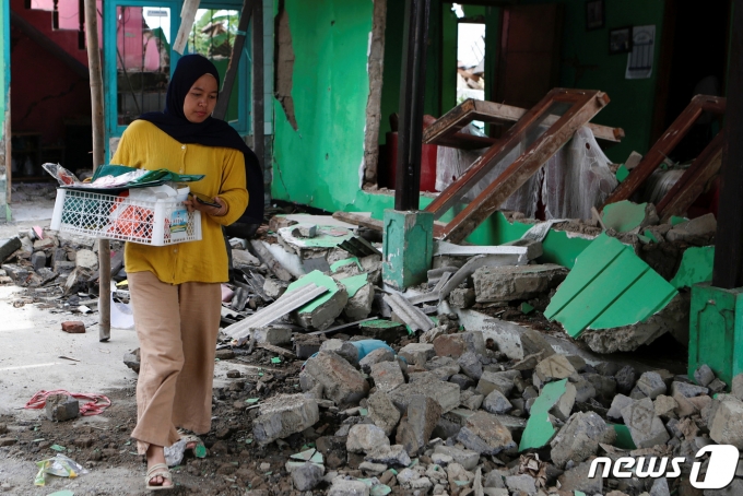 지난 24일 지진이 발생한 인도네시아 서부자바주 치안주르에서 한 주민이 소지품을 바구니에 담아 들고 무너진 건물 옆을 지나가고 있다. ⓒ 로이터=뉴스1 ⓒ News1 강민경 기자