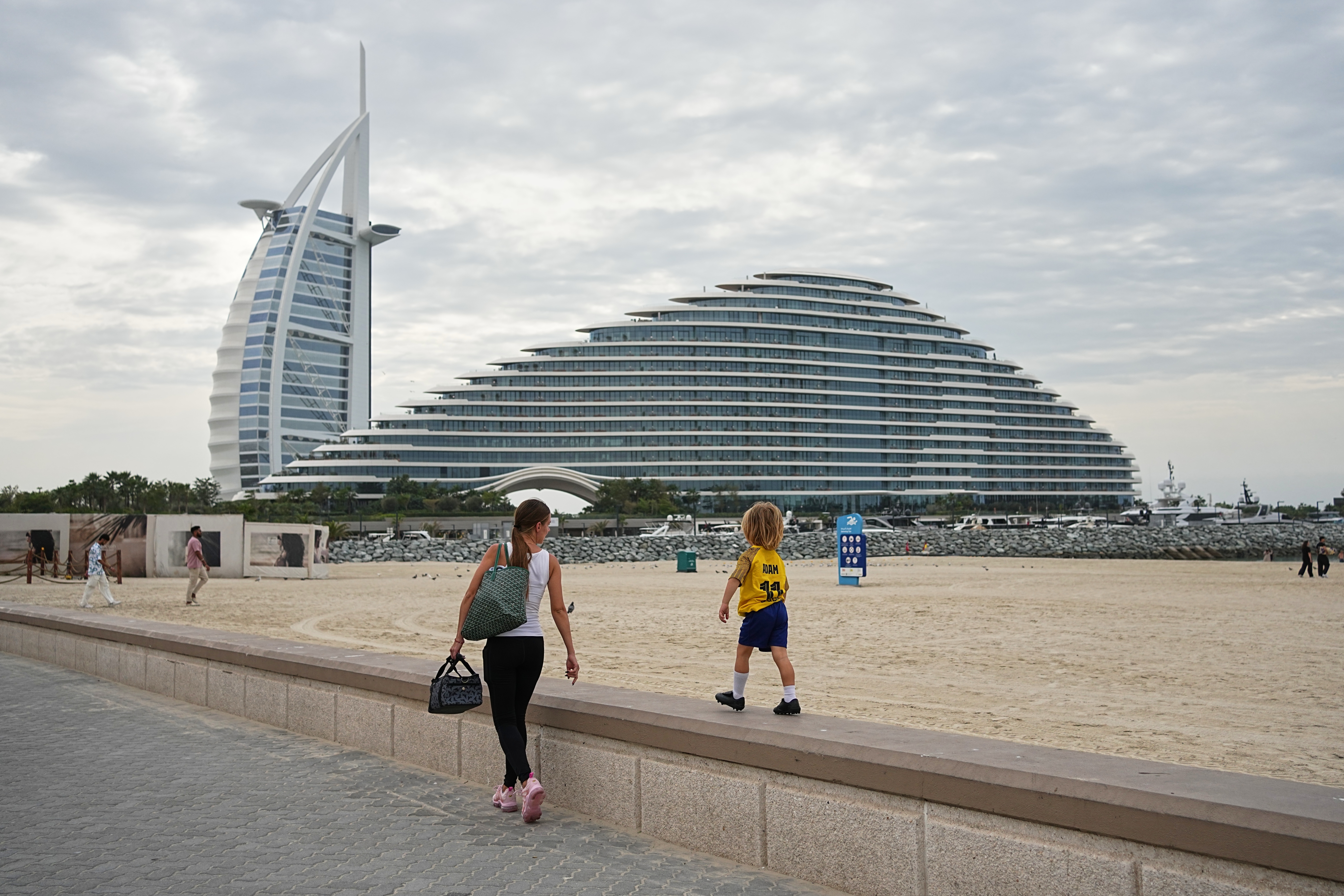 2026년 3월 12일(현지시간) 아랍에미리트(UAE) 두바이에서 한 여성과 아이가 버즈 알 아랍과 주메이라 마르사 알 아랍 호텔을 배경으로 해변을 산책하고 있다. /사진=AP/뉴시스
